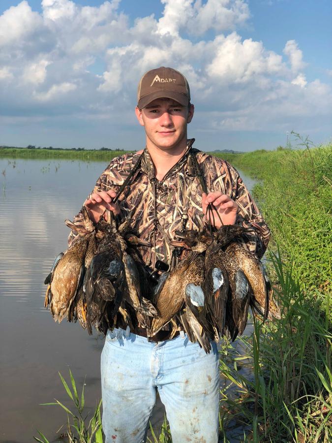 Hunter holding a full strap of gadwall and teal in the marsh