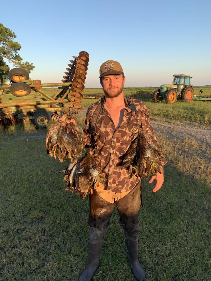 Hunter with a strap of ducks beside farm equipment at sunset