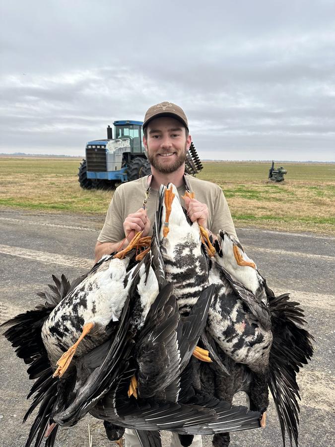 Hunter with a strap of specklebellies in front of a tractor