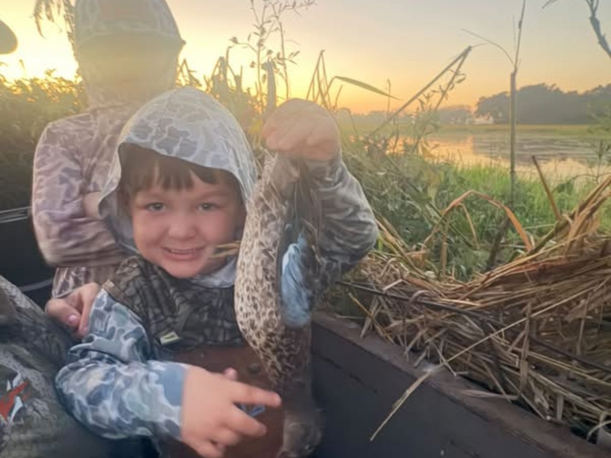 A young hunter holding up a teal in the blind at sunrise